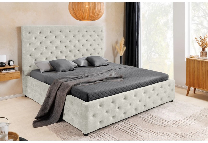 Dizajnová čalúnená manželská posteľ Kreon s vysokým obdĺžnikovým čelom a poťahom zo zamatu s chesterfield prešívaním s okrúhlymi gombíkmi v béžovej farbe šampanského s čiernymi nízkymi nožičkami a úložným priestorom