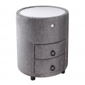 Dizajnový čalúnený okrúhly nočný stolík Aluro so sivým poťahom zo zamatu s dvomi zásuvkami a nízkymi čiernymi nožičkami s bielou vrchnou doskou s LED podsvietením