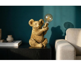 Dizajnov&aacute; zlat&aacute; art deco nočn&aacute; lampa Tierra Glam s mot&iacute;vom sediacej koaly so zdvihnut&yacute;mi predn&yacute;mi labkami držiacimi okr&uacute;hle sklenen&eacute; tienidlo s hned&yacute;m t&oacute;novan&iacute;m