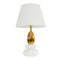 Moderná dizajnová art deco biela stolná lampa Caillou s akrylovou podstavou v tvare dvoch na sebe uložených okruhliakov so zlatou zaoblenou nohou a textilným tienidlom valcovitého tvaru s rozšírenou spodnou časťou