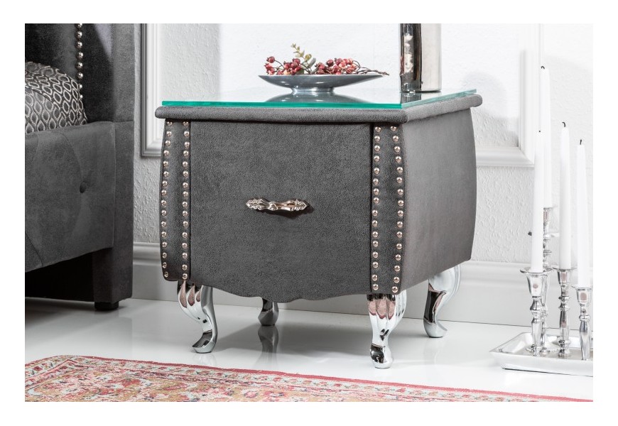 Jedinečný moderný čalúnený nočný stolík Caledonia v sivom prevedení so zásuvkou na kovovým nohách a so sklenenou doskou