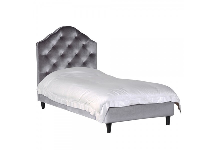 Štýlová zamatová posteľ Alcala I v sivom poťahu s Chesterfield prešívaním doplneným o hranaté nohy z dreva v čiernej farbe.