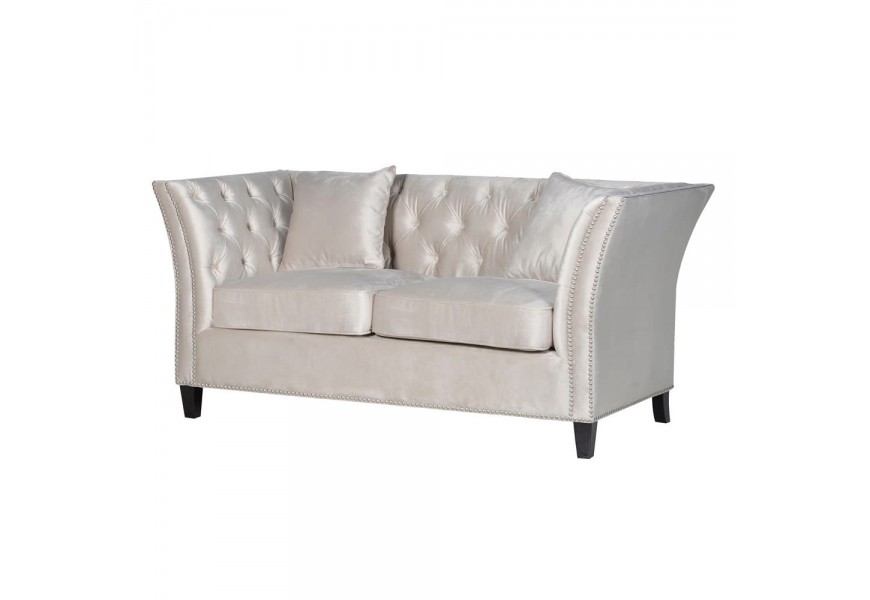 Štýlová sedačka Alevion II v bledom zamate doplnená striebornými sponkami a čiernymi nohami z dreva