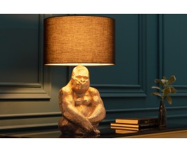 Art deco stolová lampa Apell s kovovu zlatou podstavou s dizajnom sediacej gorily a s okrúhlym látkovým čiernym tienidlom