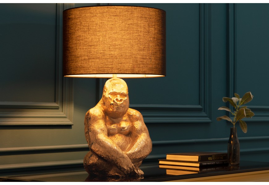 Art deco stolová lampa Apell s kovovu zlatou podstavou s dizajnom sediacej gorily a s okrúhlym látkovým čiernym tienidlom