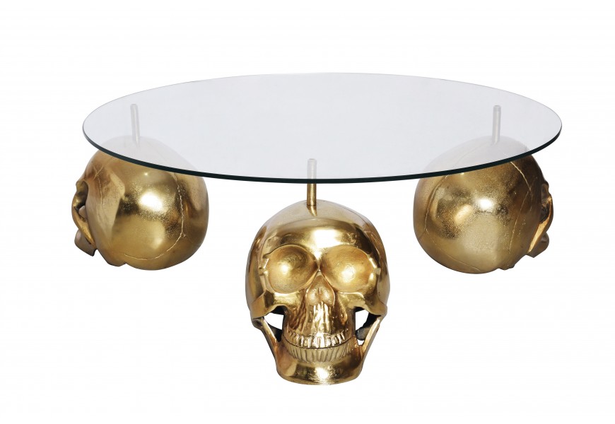 Dizajnový konferenčný stolík Hamlet s okrúhlou priehľadnou sklenenou doskou a tromi nožičkami v tvare lebiek z kovu v zlatej farbe v glamour štýle