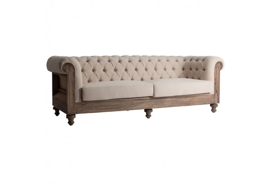 Luxusná béžová sedačka Gretchen s drevenou konštrukciou v svetlej hnedej farbe s vyrezávanými nožičkami a textilným čalúnením na opierke s ozdobným prešívaním v štýle chesterfield