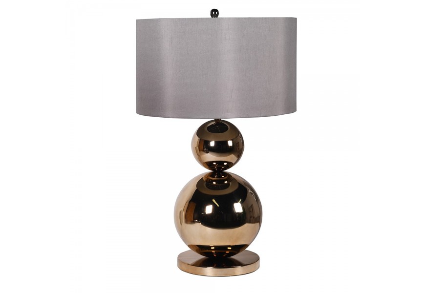 Dizajnová glamour nočná lampa Leman s nohou z kovu v zlatej farbe v podobe dvoch gulí a okrúhlej podstavy a s valcovým sivým tienidlom