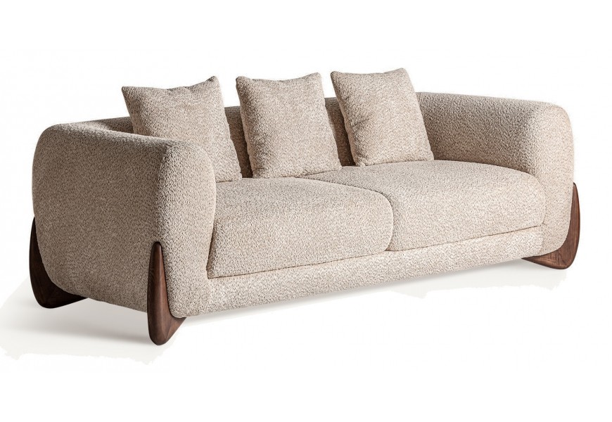 Luxusná art deco trojmiestna sedačka Leonys s bouclé poťahom v béžovej farbe s masívnymi jaseňovými drevenými nožičkami v hnedej farbe v tvare bumerangu s tromi vankúšmi