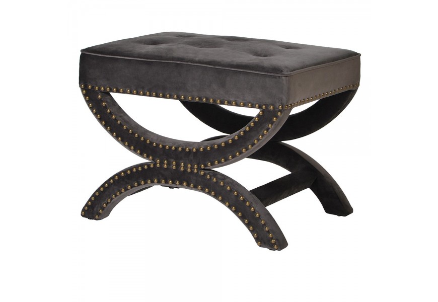 Luxusná dizajnová čalúnená taburetka s celoplošným poťahom zo zamatu v sivej farbe s obdĺžnikovým sedadlo s prešívaním s okrúhlymi gombíkmi a podstavou zdobenou kovovými nitmi v zlatej farbe s dvomi nohami v tvare X so zaoblenými líniami