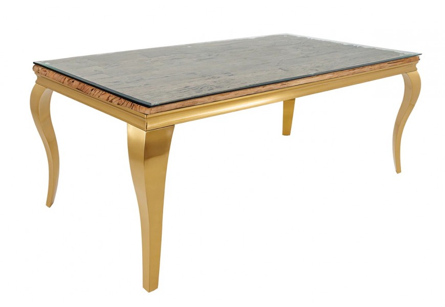 Luxusný moderný zlatý jedálenský stôl Gold Barock s kovovou konštrukciou s prehnutými kabriolovými nohami s obdĺžnikovou doskou z teakového dreva v naturálnej hnedej farbe s výraznou štruktúrou a vrchnou doskou z priehľadného bezpečnostného skla