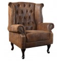 Klasické klubové kreslo s vysokým operadlom a bočnými opierkami z hnedej kože so zapustenými gombíkmi a dekoračnými kovovými nitmi na tmavých drevených nožičkách