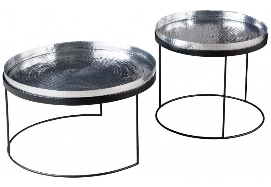 Súprava dvoch okrúhlych kovových stolíkov s lesklou kladivkovanou povrchovou úpravou v striebornej farbe a čiernou minimalistickou konštrukciou z tenkých kovových profilov.