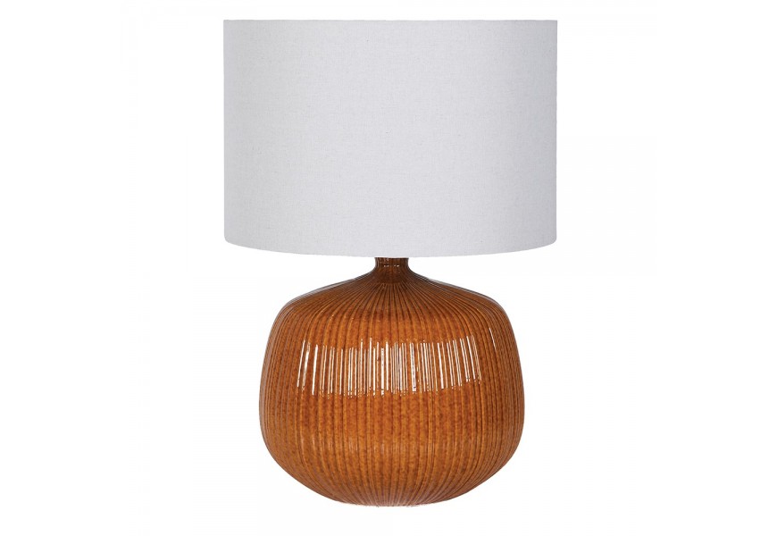 Dizajnová moderná stolná lampa Luffy s valcovitým tienidlom z ľanovej textílie v bielej farbe s prírodnou štruktúrou s okrúhlou podstavou z keramiky v karamelovej hnedej farbe s reliéfnym vertikálnym zdobením a lesklou glazúrou